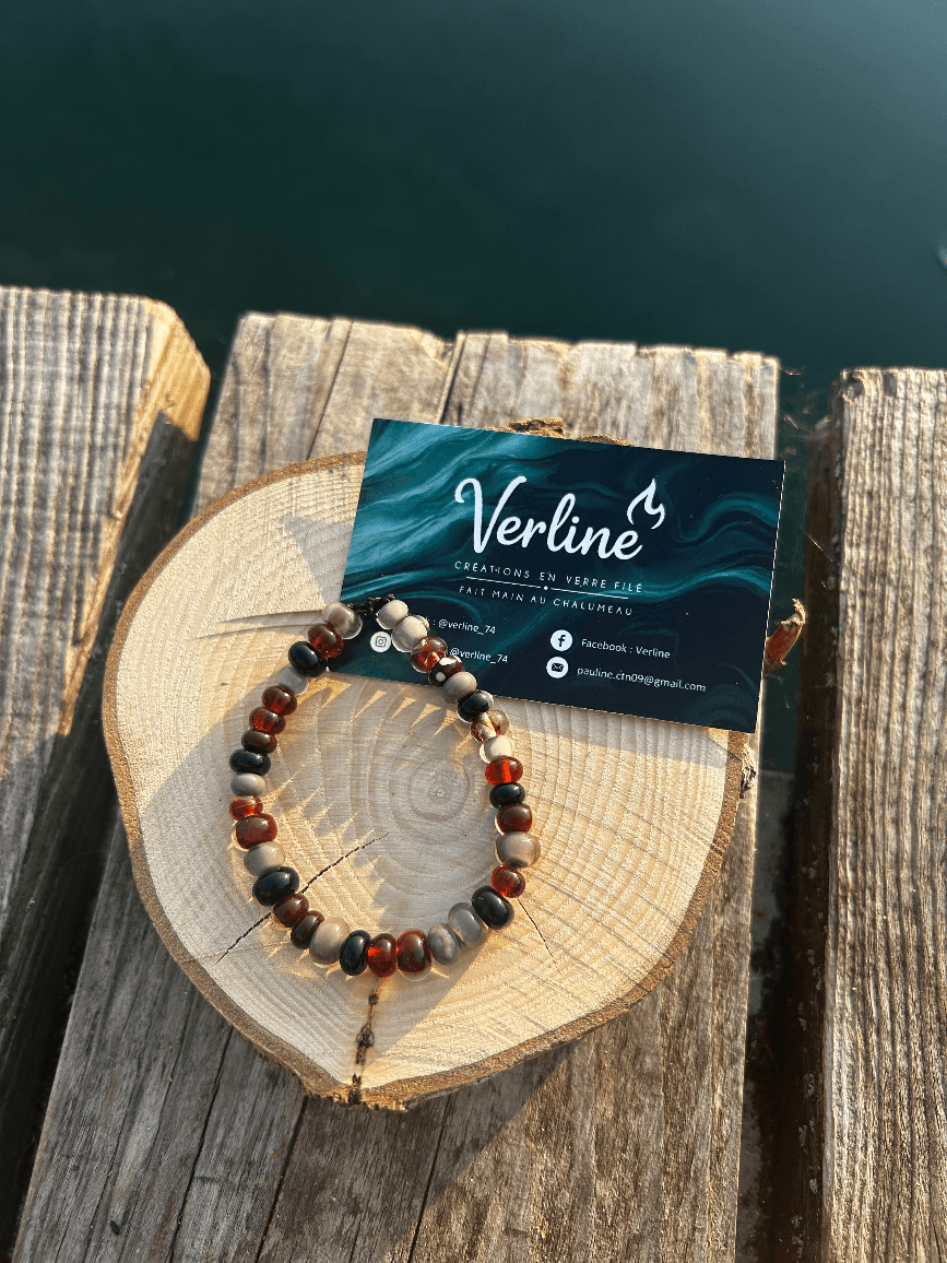 Bracelet en perles de verre ambrées et grises posé sur une rondelle de bois au bord de l'eau