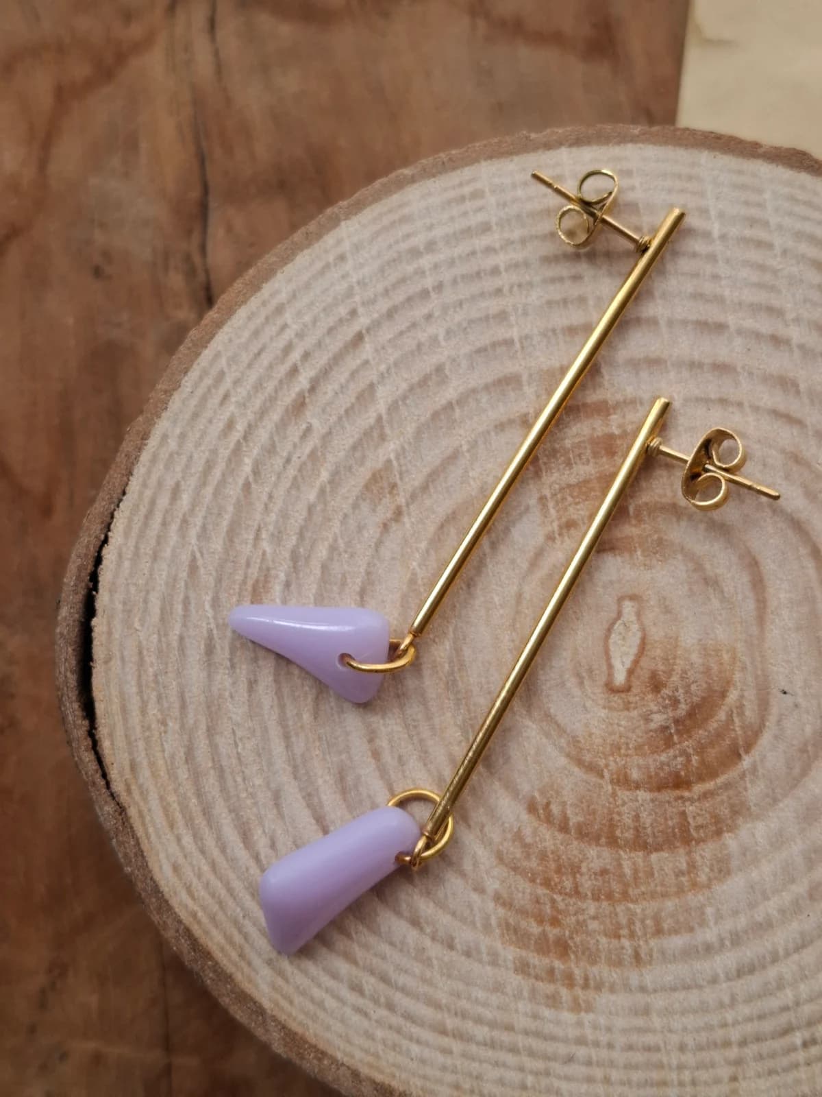 Paire de boucles d'oreilles pendantes dorées avec pendentifs violets posée sur un rondin de bois.