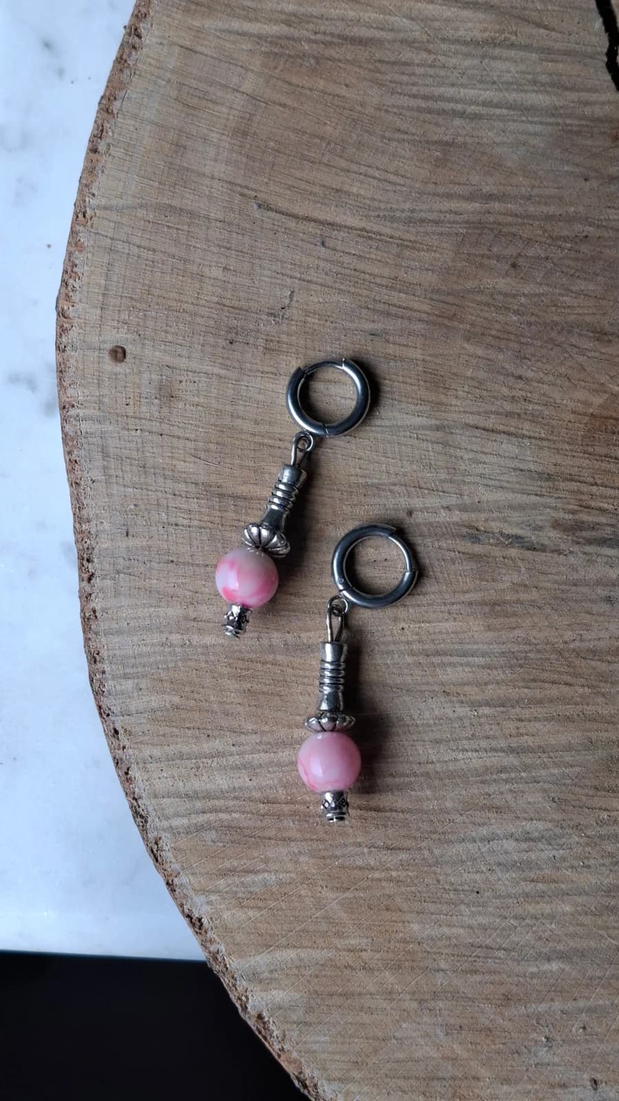 Paire de boucles d'oreilles suspendues à anneaux argentés avec perle rose marbrée et pampille ciselée.