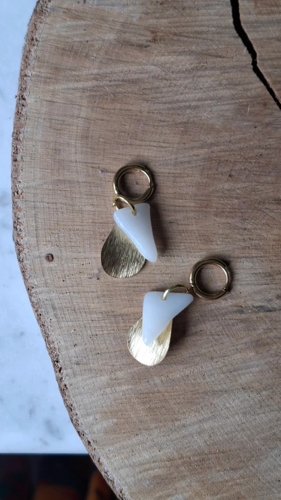 Boucles d'oreilles en verre blanc et pampilles dorées posées à plat sur un support en bois
