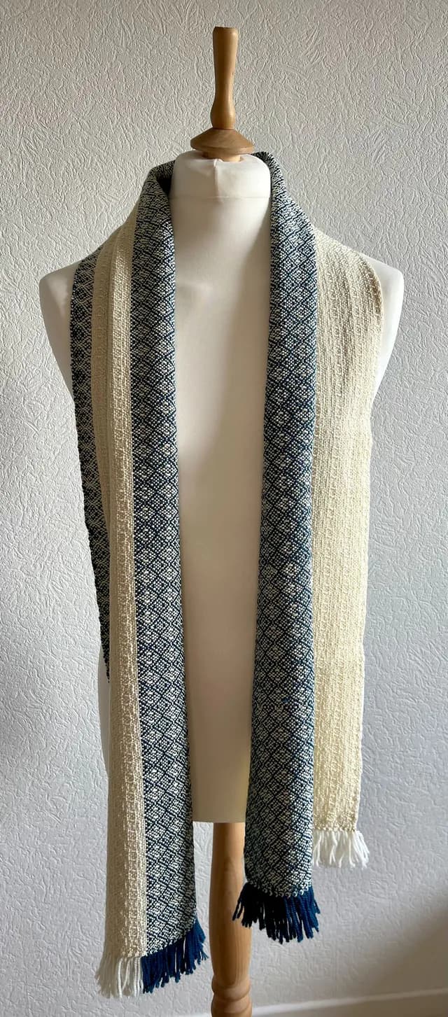 Écharpe bicolore bleue et beige à motifs géométriques et franges, portée sur un buste de mannequin.