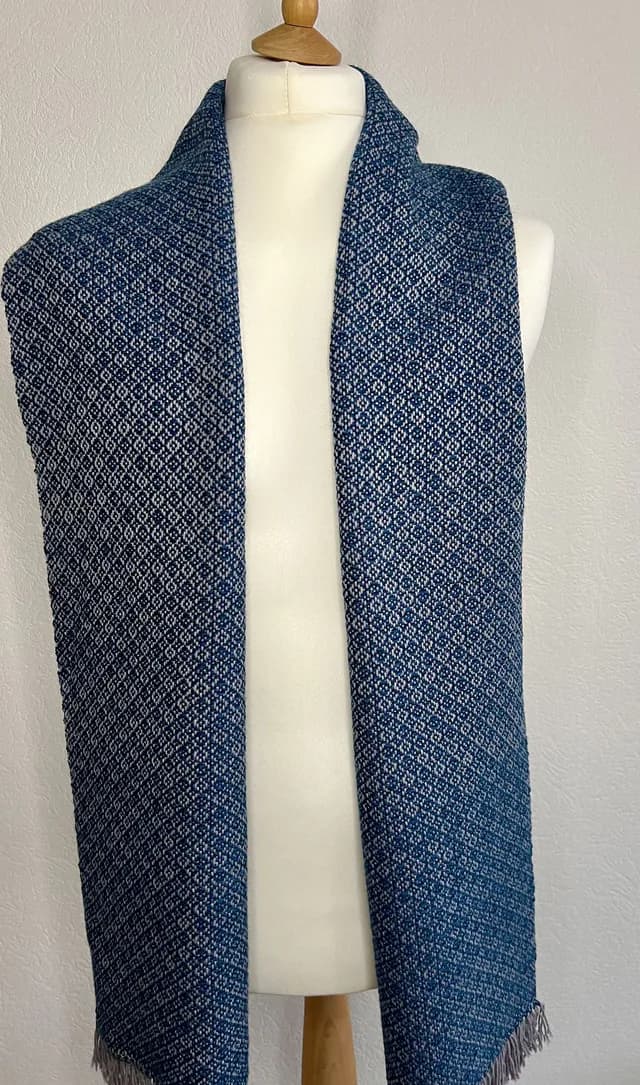 Écharpe tissée bleue et grise à motifs géométriques drapée sur un mannequin de couture.
