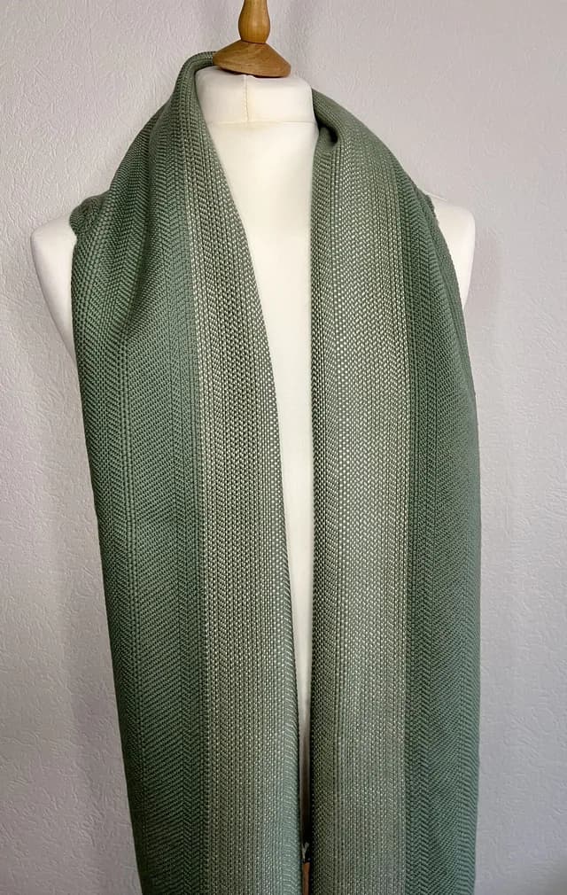 Écharpe vert sauge tissée à la main drapée sur un mannequin de couture blanc.