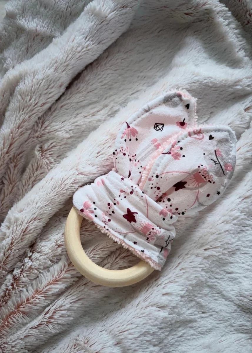 Anneau de dentition en bois avec tissu imprimé rose poudré noué en oreilles de lapin sur plaid doux.