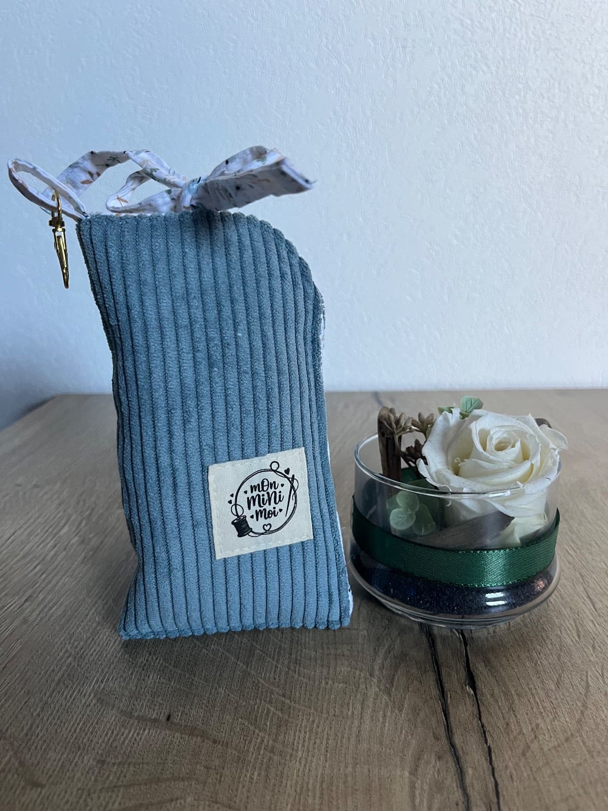 Étui à lunettes en velours côtelé bleu jean posé à côté d'une rose blanche décorative.