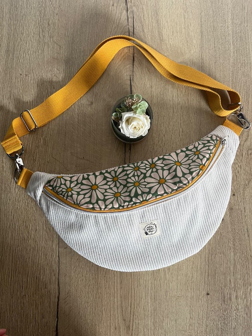 Sac banane en velours côtelé crème avec rabat à motif fleuri et sangle jaune moutarde posé à plat.
