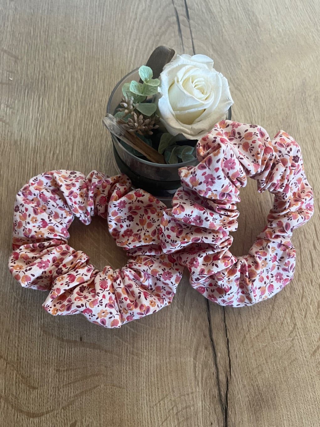 Chouchous froncés à motif floral rose et bordeaux posés près d'une rose blanche.