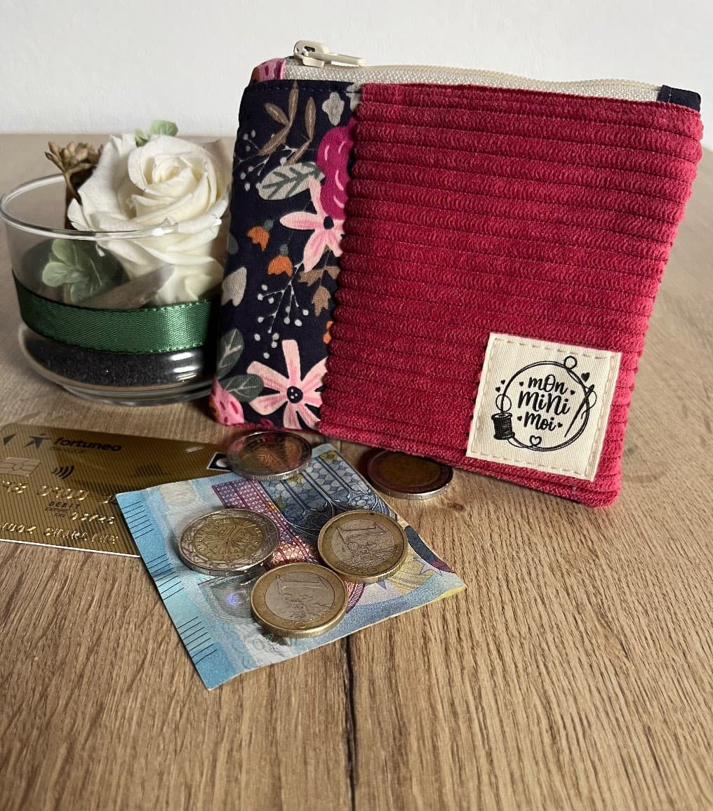 Porte-monnaie en velours côtelé framboise et tissu fleuri foncé posé près de pièces de monnaie