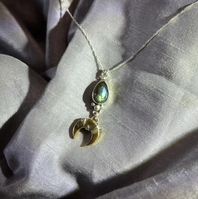 Pendentif en labradorite et croissant de lune en laiton sur tissu drapé gris aux reflets lumineux