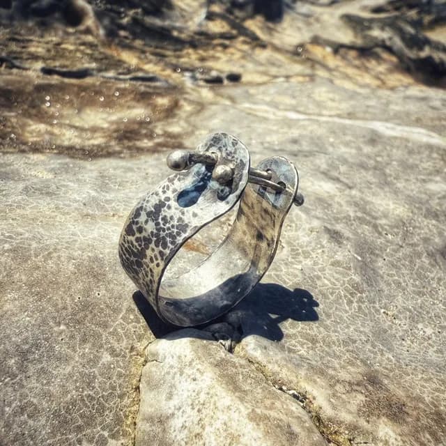 Bague Catakomb en argent texturé avec deux tiges mobiles, posée sur une roche claire