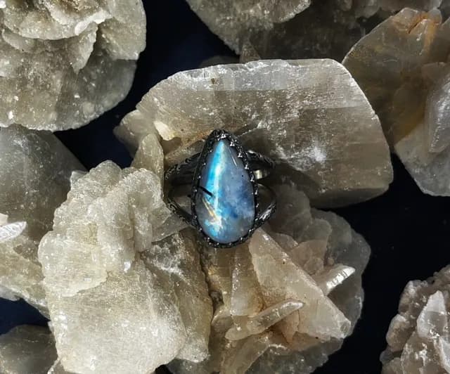 Bague en argent ornée d'une pierre de lune taillée en goutte posée sur un bloc minéral.
