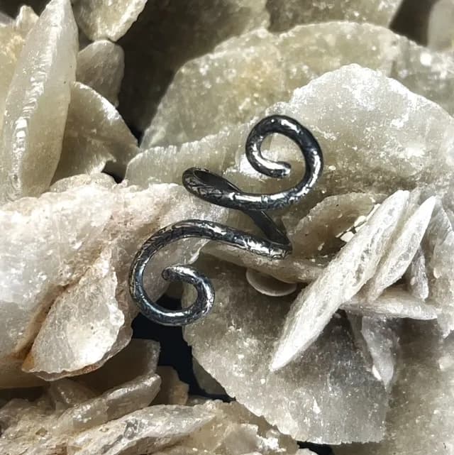 Bague de phalange réglable en argent 925 aux extrémités en spirales, posée sur une roche cristalline.