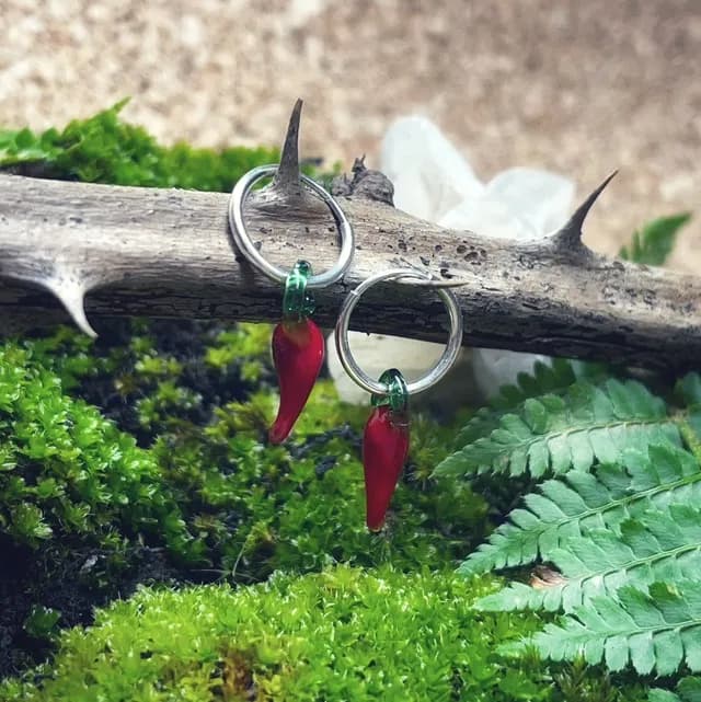 Créoles en argent ornées de piments rouges en verre suspendues à une branche d'épines.