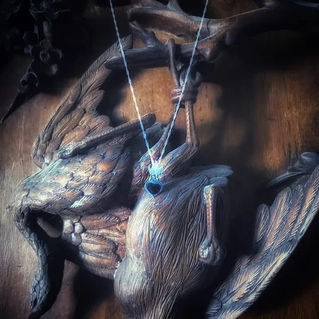Collier avec pendentif sacré cœur en argent et émail noir suspendu devant une sculpture en bois.