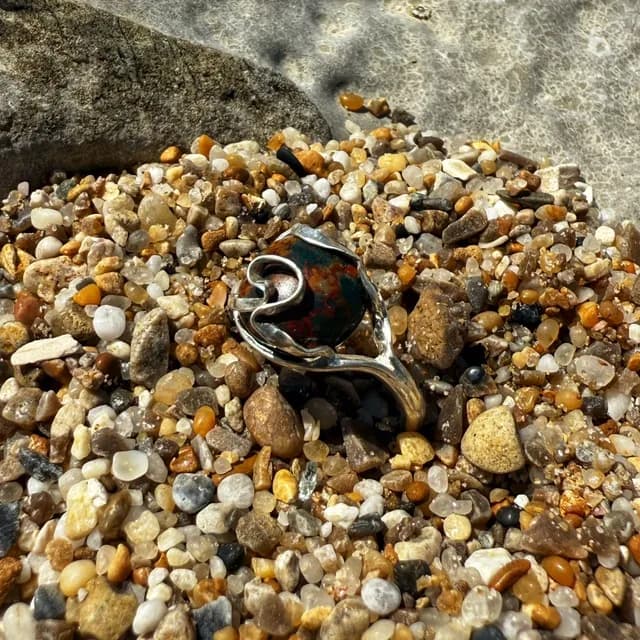 Bague en argent avec pierre jaspe océan posée sur un lit de petits galets de plage.