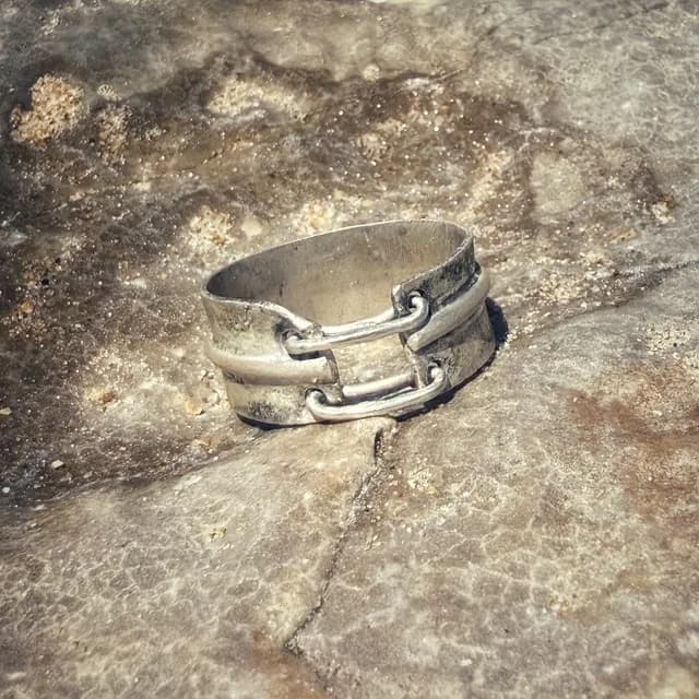 Bague large en argent texturé avec deux anneaux mobiles, posée sur une roche