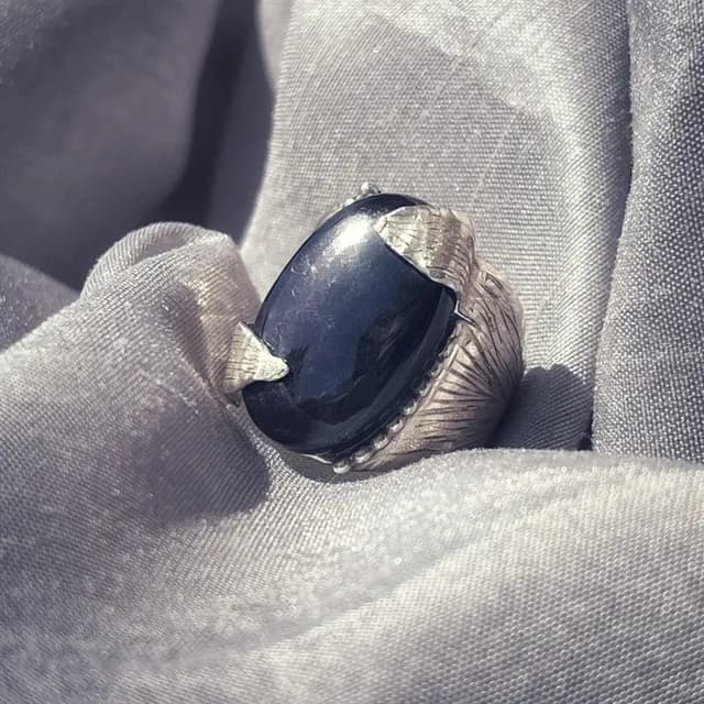 Bague en argent gravé sertie d'une purpurite sombre ovale, posée sur un tissu satiné gris