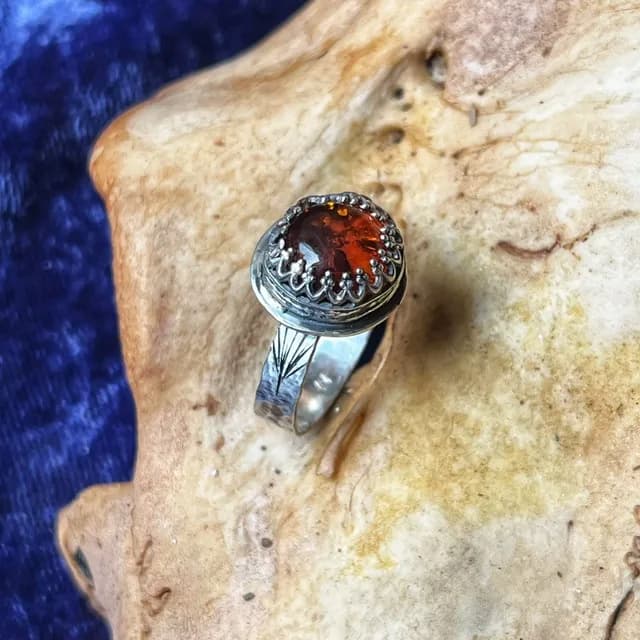 Bague en argent avec cabochon rond en ambre orangé serti dans une bordure travaillée.