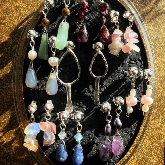 Assortiment de puces d'oreilles pendantes en argent avec diverses pierres et perles de couleurs sur fond noir.