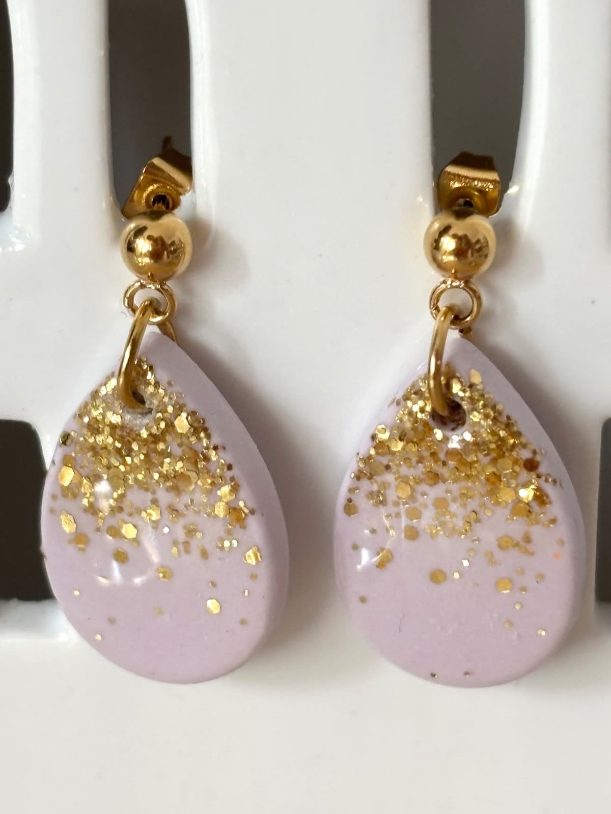 Boucles d'oreilles pendantes lilas en forme de goutte avec paillettes dorées sur présentoir blanc