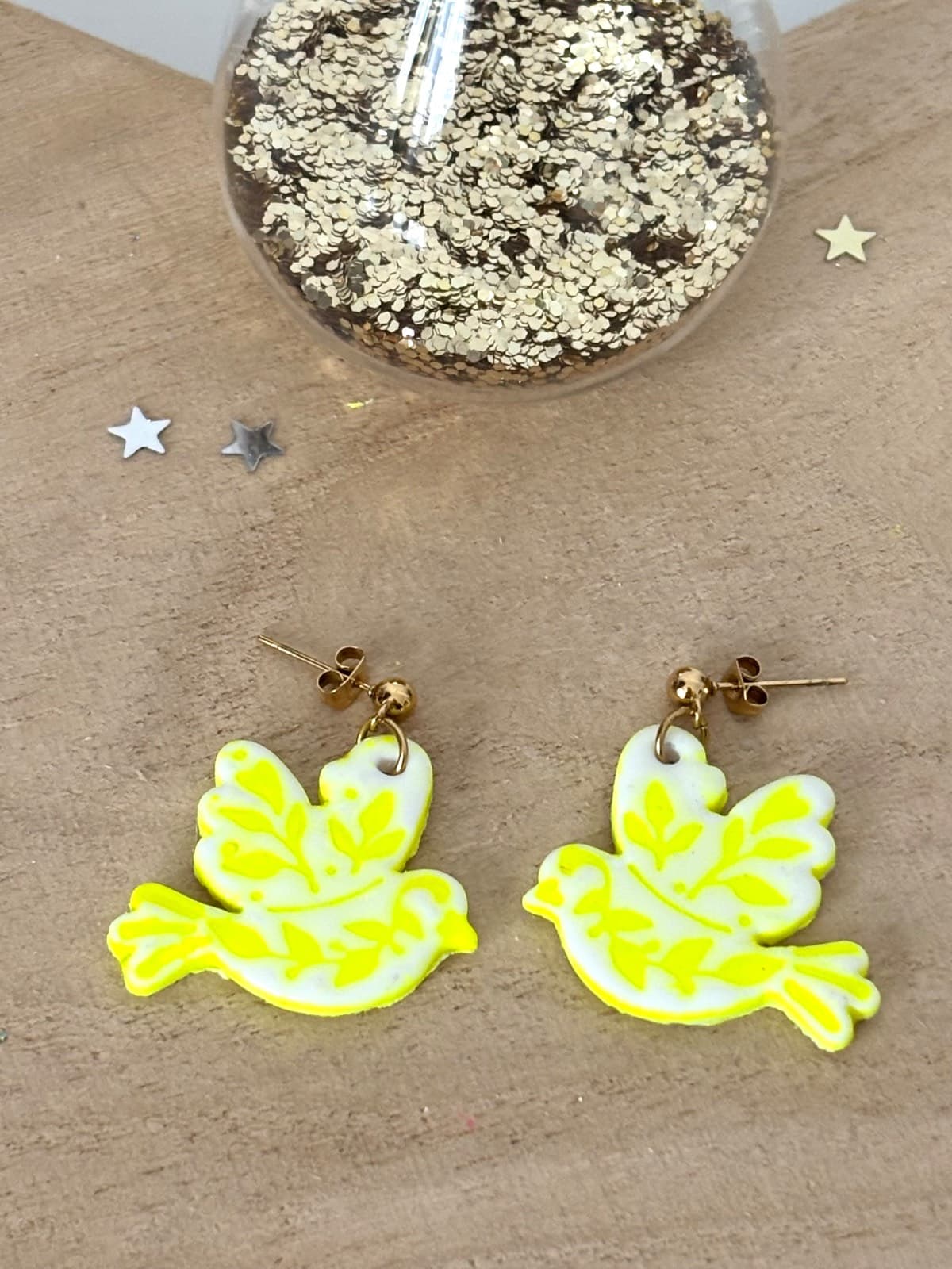 Paire de boucles d'oreilles pendantes oiseau blanc et motifs végétaux jaune néon sur fond bois
