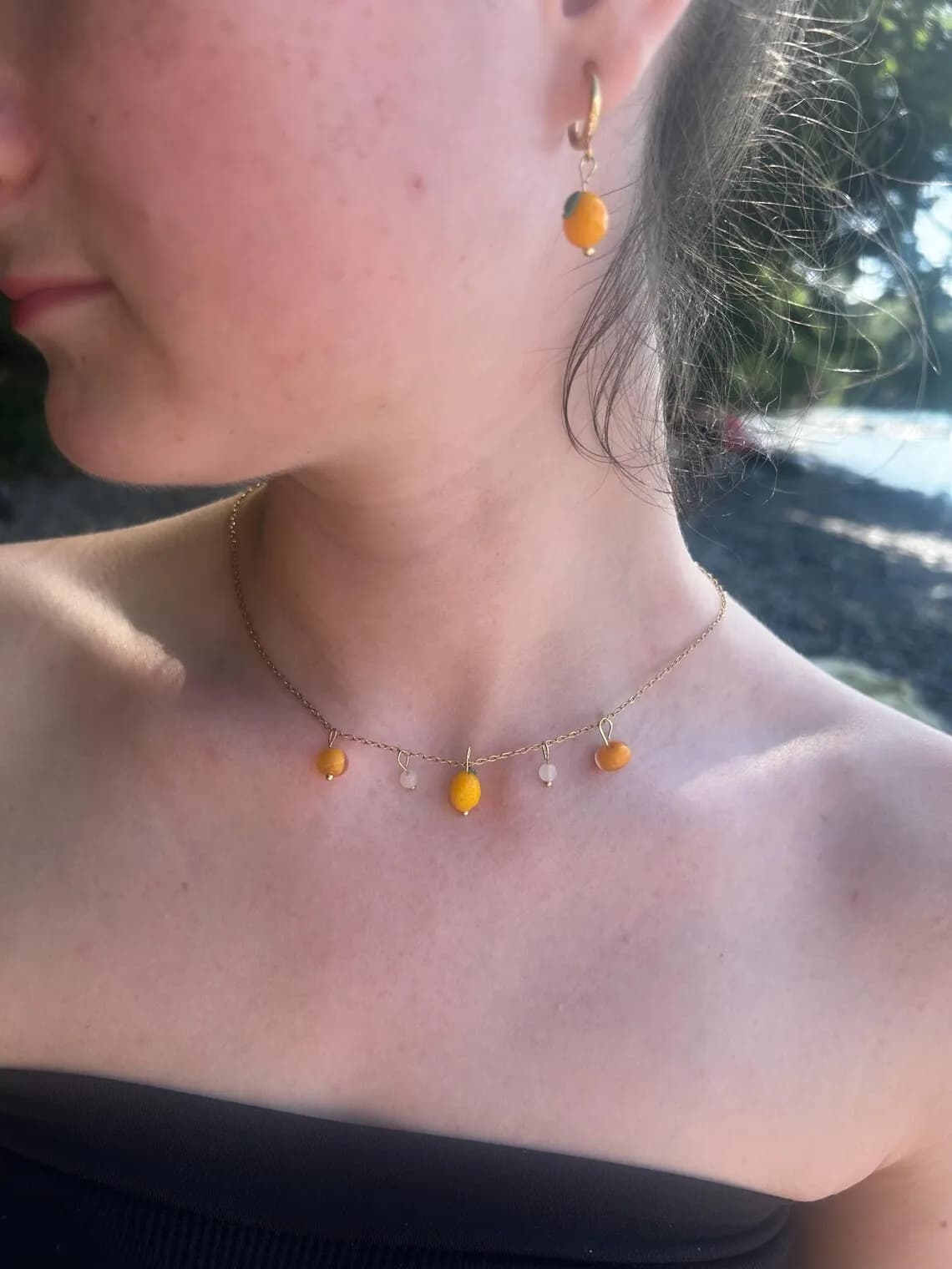 Collier à breloques citrons jaunes présenté sur un buste d'exposition devant la mer.