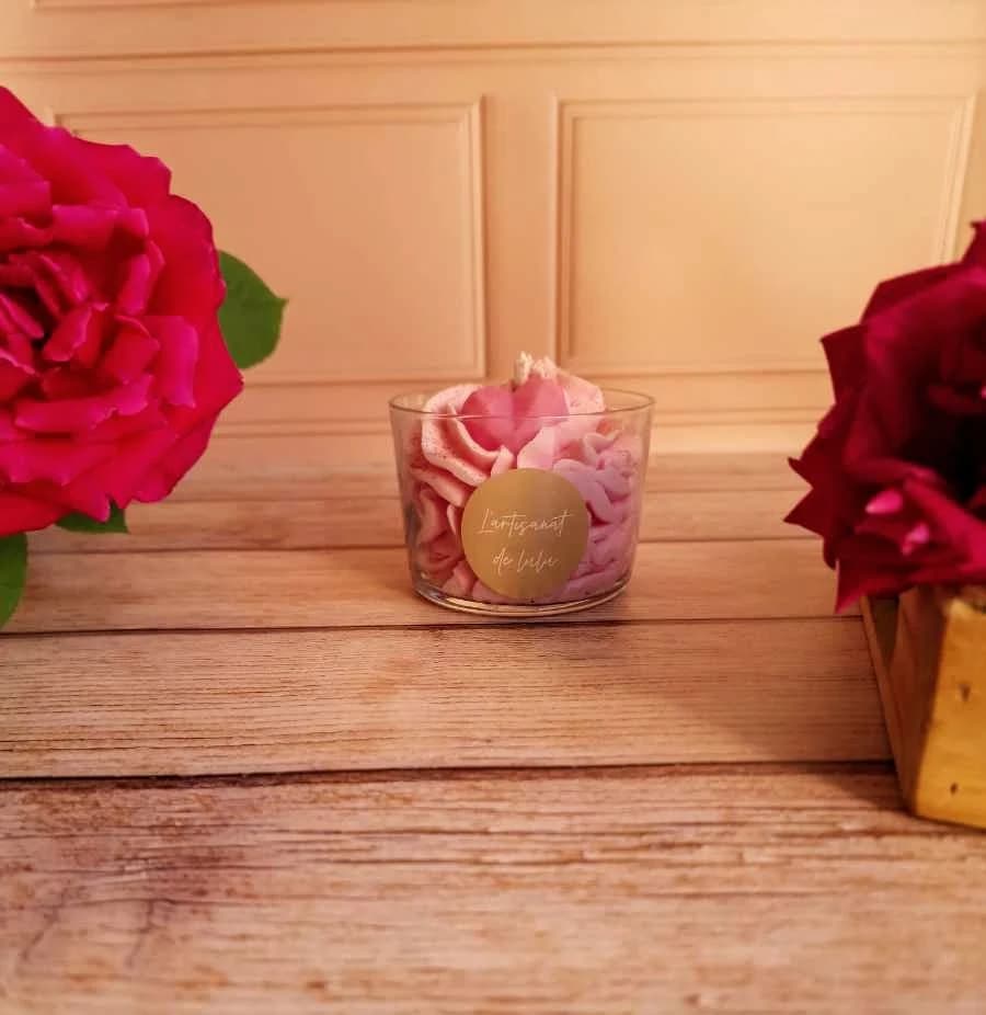 Bougie en verre avec cire rose texturée en chantilly et petit cœur, posée entre deux roses