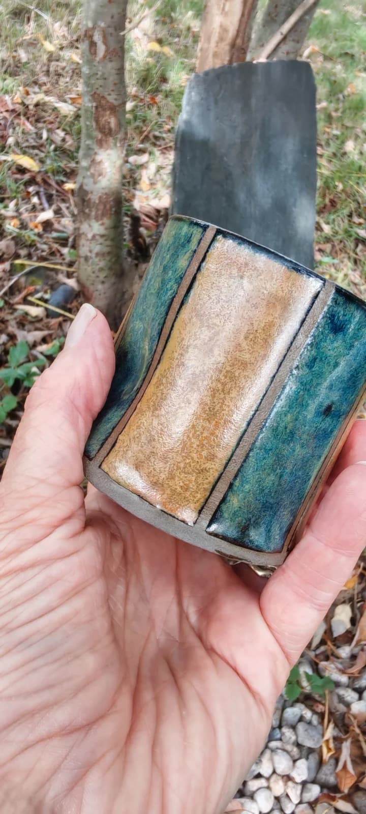 Gobelet sans anse aux bandes verticales bleu, vert et ocre tenu dans la main.