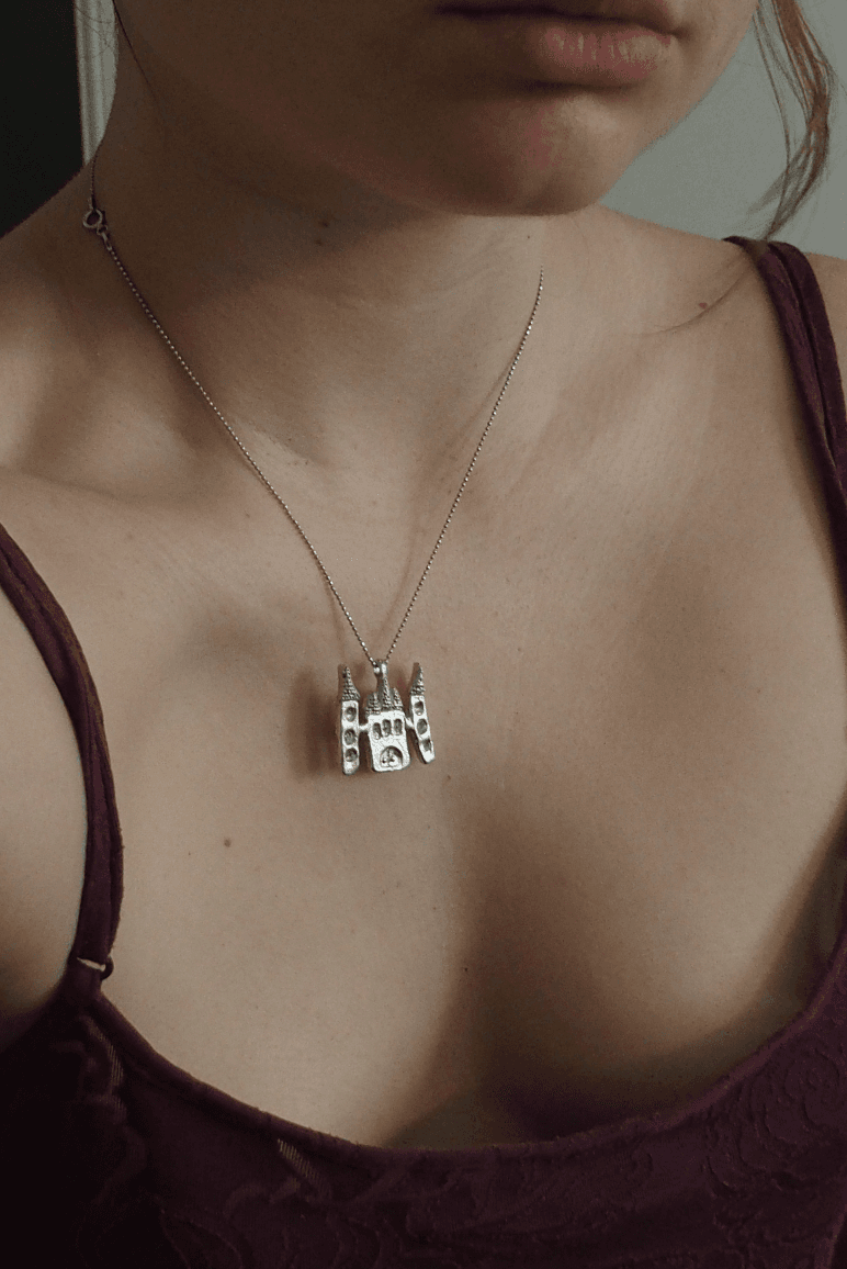 Pendentif en étain en forme de château aux trois tours ajourées porté au cou sur une fine chaîne.